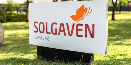 Skilt hvor der står Solgaven Næstved og med en sommerfugl med en græsplæne bagved