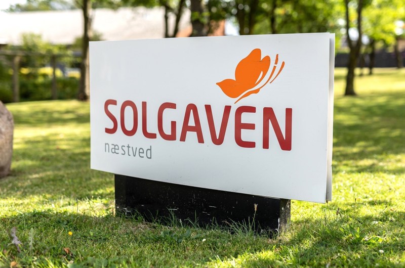 Skilt hvor der står Solgaven Næstved og med en sommerfugl med en græsplæne bagved