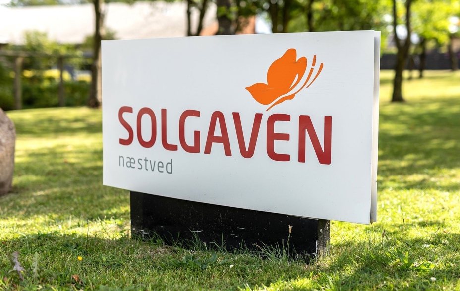 Skilt hvor der står Solgaven Næstved og med en sommerfugl med en græsplæne bagved