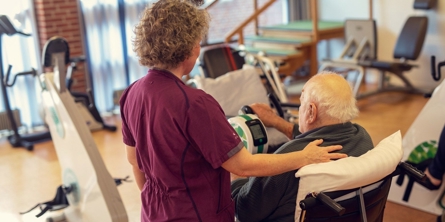 Medarbejder på Solgaven står ved beboer, der sidder ned og cykler. Støtter med hånden på ryggen.