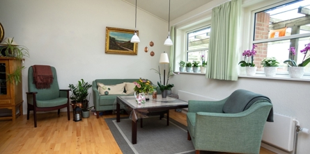 En bolig på Solgaven Næstved. En sofa, 2 stole i en grønlig farve samt et sofabord. Et tæppe under border, lamper over sofabord.2 vinduer med gardiner